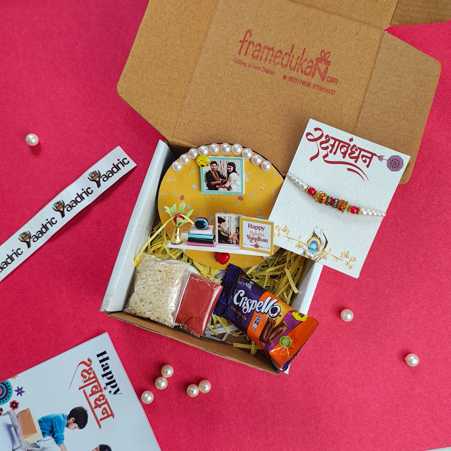 Gift box with Rakhi, cards, and snacks on a red background
