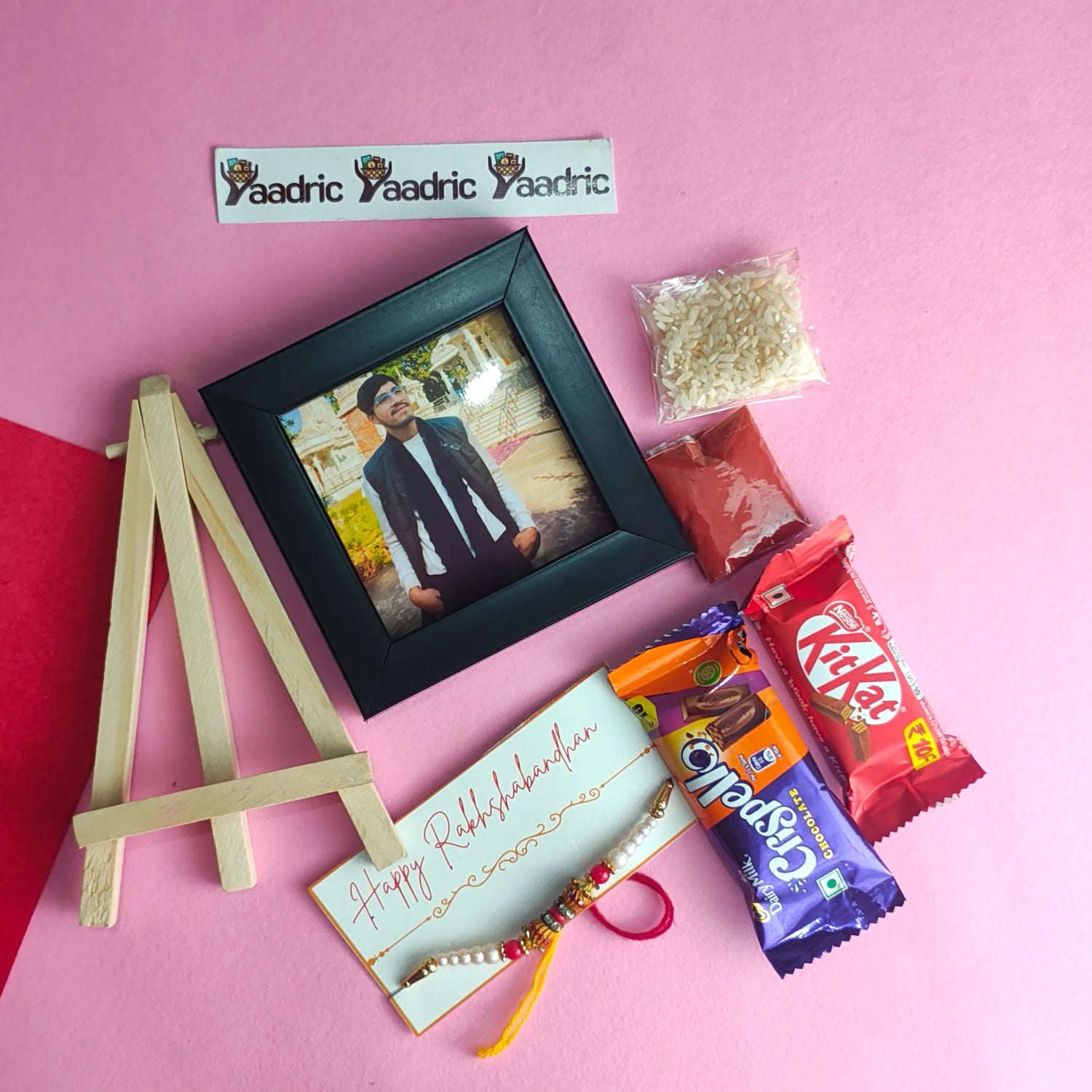 Small photo frame with a man's portrait, a small wooden easel, and candy bars on a pink background.
